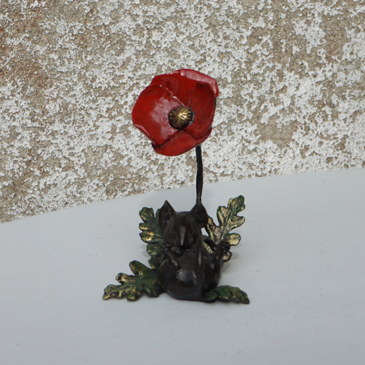 Small red flower and green plant on a textured surface with a white background